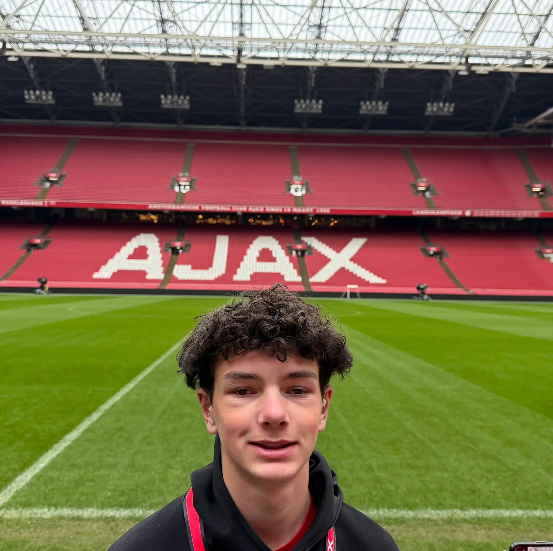 Daylen Hammon selfie on the pitch at Johan Cruyff Arena with AJAX spelled out in red seats behind him, Amsterdam 2026